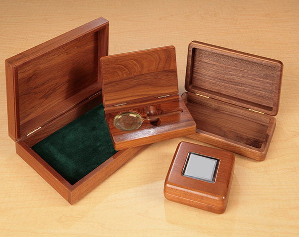 Higher end custom wood hinged top walnut boxes with cutouts to hold item place and felt liners. One of the examples shows a magnifying glass.